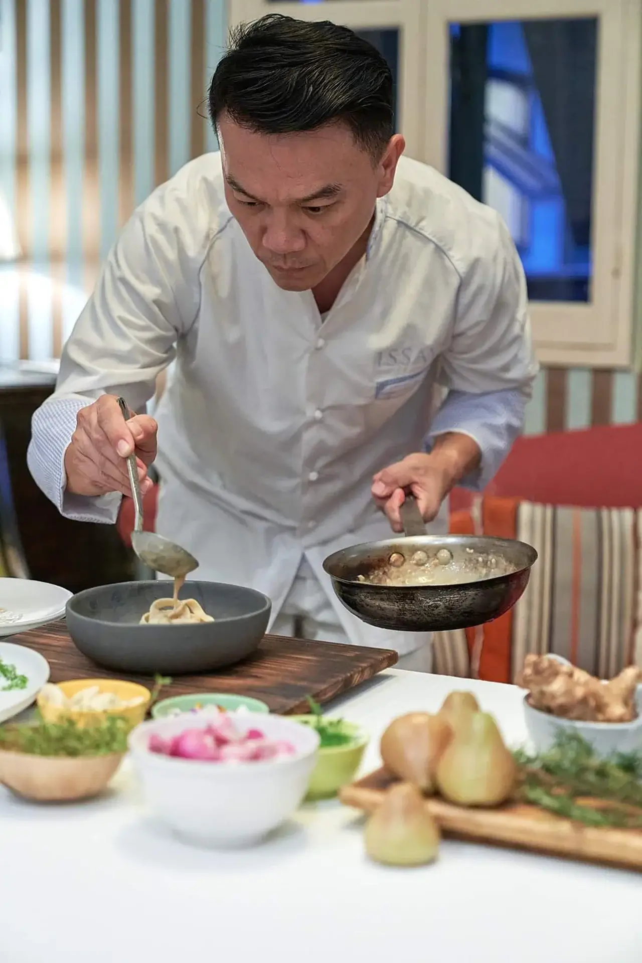 Ian leaning over a meal pouring sauce onto pasta