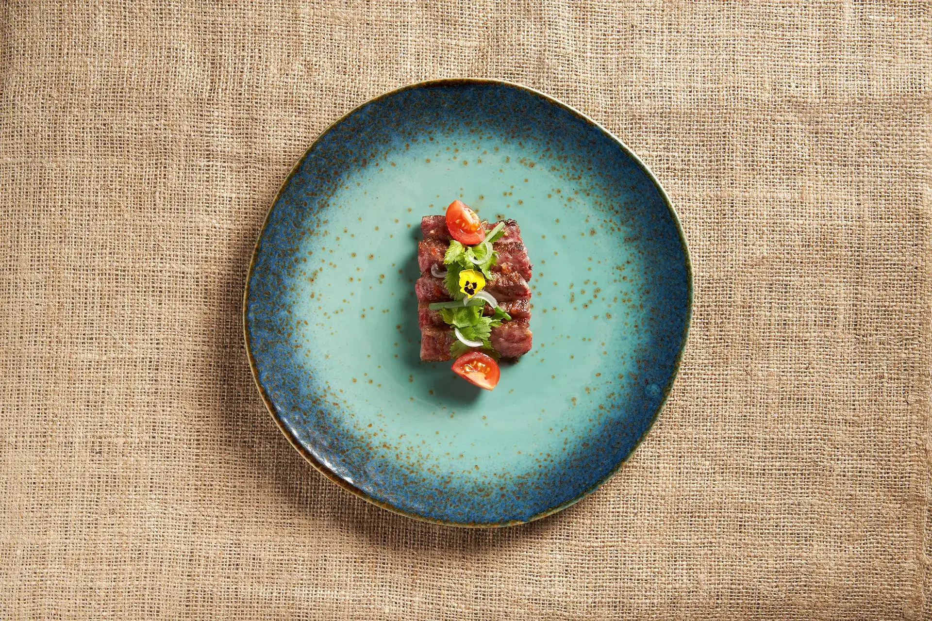 A dish made by Ian on a green ceramic plate which sits on a burlap cloth