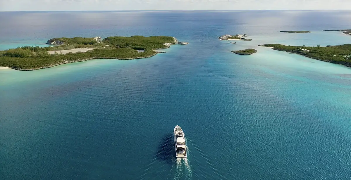 Aerial view of a boat leaving a wake as it travels between small green islands in clear blue water.